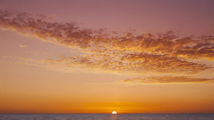 Fototapeta premium Breathtaking view of a vibrant sunset over the ocean, with the sun on the horizon and stunning clouds illuminated in warm orange and pink hues