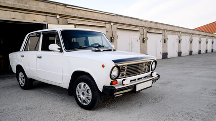 side view of a white retro car parked in a parking lot near auto garages