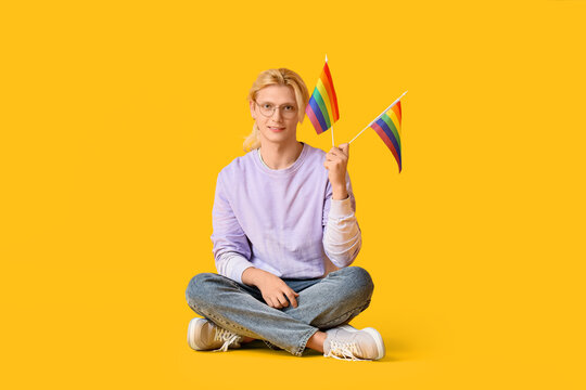 Young man with LGBT flags sitting on yellow background - Powered by Adobe