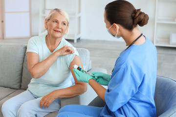 Obraz premium Senior woman receiving vaccine from doctor at home