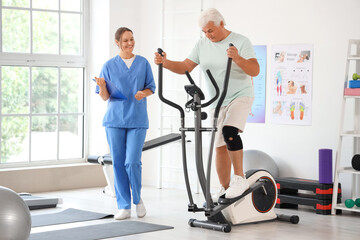 Senior man exercising on elliptical machine with therapist in rehabilitation center