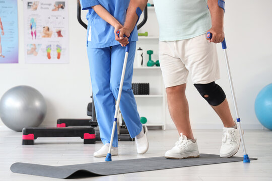 Senior man with crutches and therapist walking in rehabilitation center - Powered by Adobe