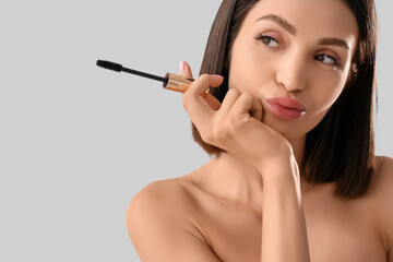 Fototapeta premium Thoughtful young woman with mascara on light background, closeup
