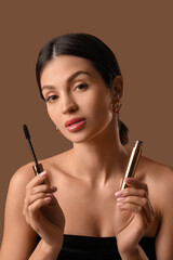 Fototapeta premium Beautiful young woman with mascara on brown background, closeup