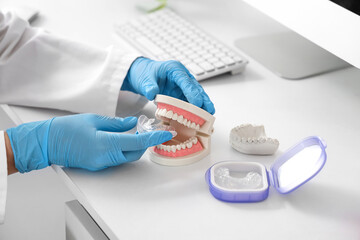 Female dentist with occlusal splint and jaw model at desk in office, closeup