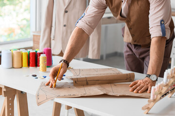 Male tailor working with pattern at table in atelier