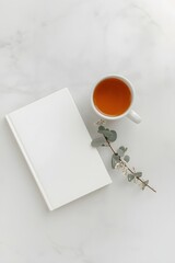 Minimal flat lay composition with blank white book cover, hot cup of tea, and eucalyptus leaves on marble background, ideal for mockup, branding, design, or minimalist lifestyle concept