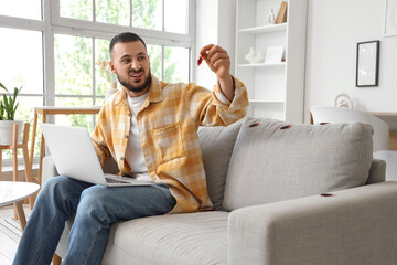 Displeased young man with laptop and cockroaches on sofa at home