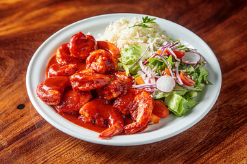 A plate of camarones a la diabla, spicy shrimp cooked in a rich red sauce, served with white rice and a side salad.