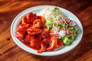 A plate of camarones a la diabla, spicy shrimp cooked in a rich red sauce, served with white rice and a side salad.