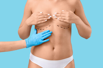 Hand of doctor and young woman with marking on breast against blue background. Plastic surgery...