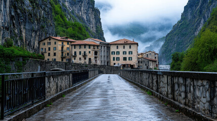 Scenic view of historic buildings nestled between towering cliffs with misty clouds, in a tranquil valley setting with a narrow road leading to the structures