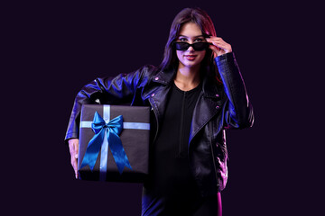 Young woman in sunglasses with gift box on dark background. Cyber Monday