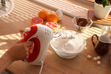 Female hand whipping egg whites with mixer on table in kitchen