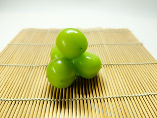 A vibrant cluster of fresh green grapes, bursting with sweet flavor, elegantly presented on a rustic bamboo mat, offering a wholesome and refreshing natural snack