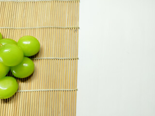 Fresh vibrant green grapes on a bamboo mat with a clean white background, ideal for healthy eating concepts and design