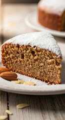A slice of almond cake with powdered sugar and almonds on a white plate on a wooden surface