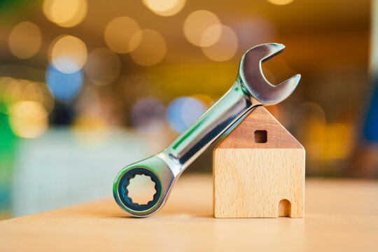 Metal wrench leaning on wooden house model, symbolizing home repair, maintenance service, DIY renovation, construction, and real estate improvement. Ideal for housing and handyman concept visuals.