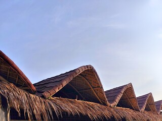 Wavy Detailed Thatched Roof Structure with Blue Sky Above and Power Lines