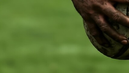 Mud Covered Hands Holding Rugby Ball Close Up Green Field Background
