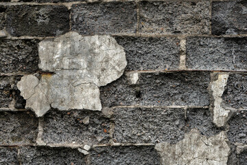 Fototapeta premium A textured view of a deteriorating stone wall with cracked, peeling plaster, showing layers of wear and age, highlighting urban decay and rustic architectural details
