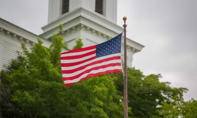 USA flag against a white building and greenery on overcast day