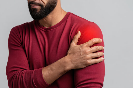 Man with shoulder pain holding his left arm, wearing red long sleeve shirt, showing discomfort and muscle ache in close up view