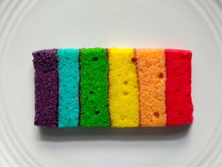 Colorful rainbow sponge cake slice served on a white plate.