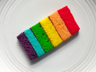 Colorful rainbow sponge cake slice served on a white plate.