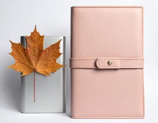 Elegant pink planner and dried maple leaf on white background.