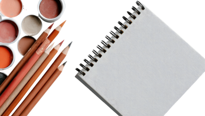 Assorted art supplies, including colored pencils and eyeshadow palettes, beside a blank notebook