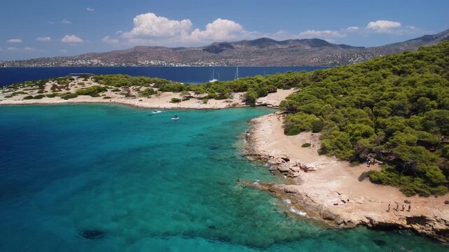 Slow drone flyback over a scenic Greek island near Aegina. Aerial drone footage showcasing the turquoise Aegean Sea, a secluded beach, and lush pine trees on a picturesque Greek island.