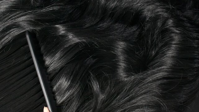 Closeup black hair texture, slow motion of female hand combing long curly hair