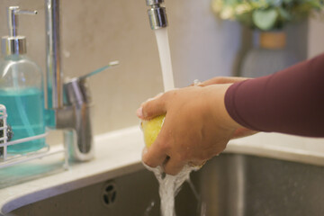 A person is rinsing a lemon under clear water at the sink