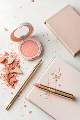 A flat lay of makeup products and a notebook on a white surface with scattered glitter