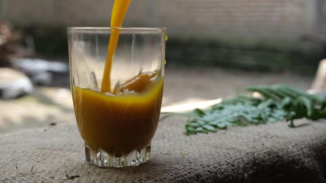 Close-up of kunyit asam, a traditional Indonesian turmeric and tamarind herbal drink, being poured into a clear glass outdoors.
