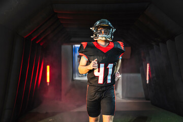 American football player running through a dark stadium tunnel, lights illuminating the path to the field. Game day preparation © Koldo_Studio