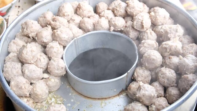 A close-up view of freshly prepared bakso meatballs being kept warm in a round metal steamer.