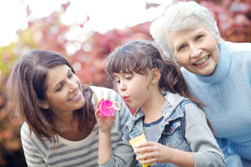 Grandma, kid and blowing bubbles with mom outdoor for play, bonding and care with bokeh. Park, family and girl with soap toy for game, mother and portrait of grandparent with happy generations