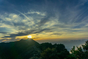 scenic view of a mountain range at sunrise, with the sun peaking over the peaks, casting a golden glow on the clouds and landscape.