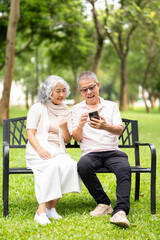 Fototapeta premium Senior couple sitting on a park bench with wheelchair is parked nearby, sharing a smartphone enjoying a peaceful spring day outdoors in a cozy and loving moment.