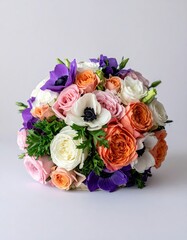 A lush, round bouquet of peach, pink, white, and purple roses and anemones, arranged with greenery, sits on a light gray background