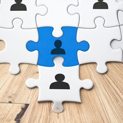 A blue puzzle piece, featuring a person icon, fits among white pieces with similar icons, all on a wood surface