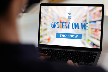 Hand using laptop computer with grocery online shopping over blur supermarket on screen background, business and technology, lifestyle concept