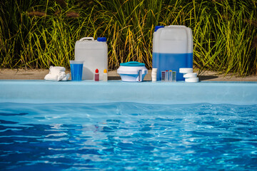 Swimming pool cleaning products with chemical canisters, chlorine tablets, measuring cup, liquid test kit and floating dispenser arranged on poolside © StockMediaSeller