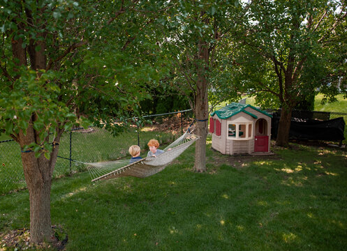 Playful kids enjoying hammock time together in shady backyard garden
