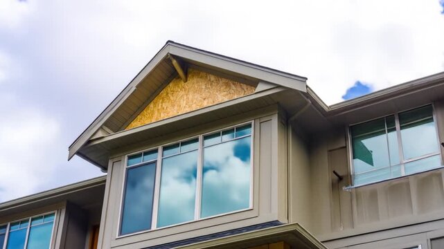 House with a light taupe exterior, large windows, and a partially visible roof under construction