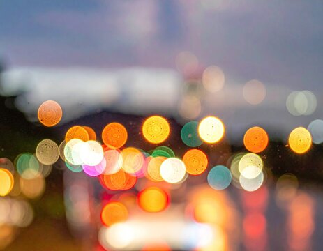 Blurred cityscape at dusk, showing multicolored bokeh from distant lights and vehicles, possibly viewed through a wet window