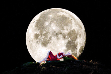 Composite, Digital artwork, of a Beautiful woman with long red hair, lying down on a rocky bed, silhouetted by a full moon © DavidOsborne
