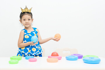 The girl wearing the crown is playing the color ball and the color ring on the white background.